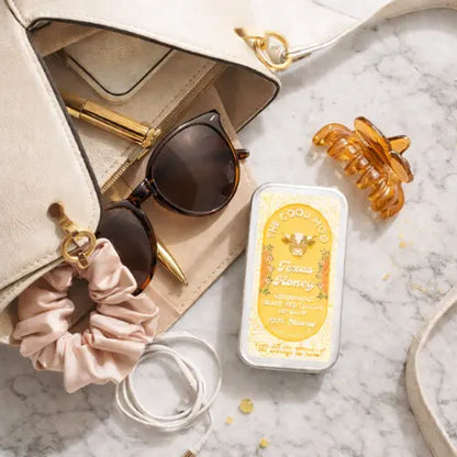 Accessories including sunglasses, scrunchie, and hair clip on a marble surface with a product container.